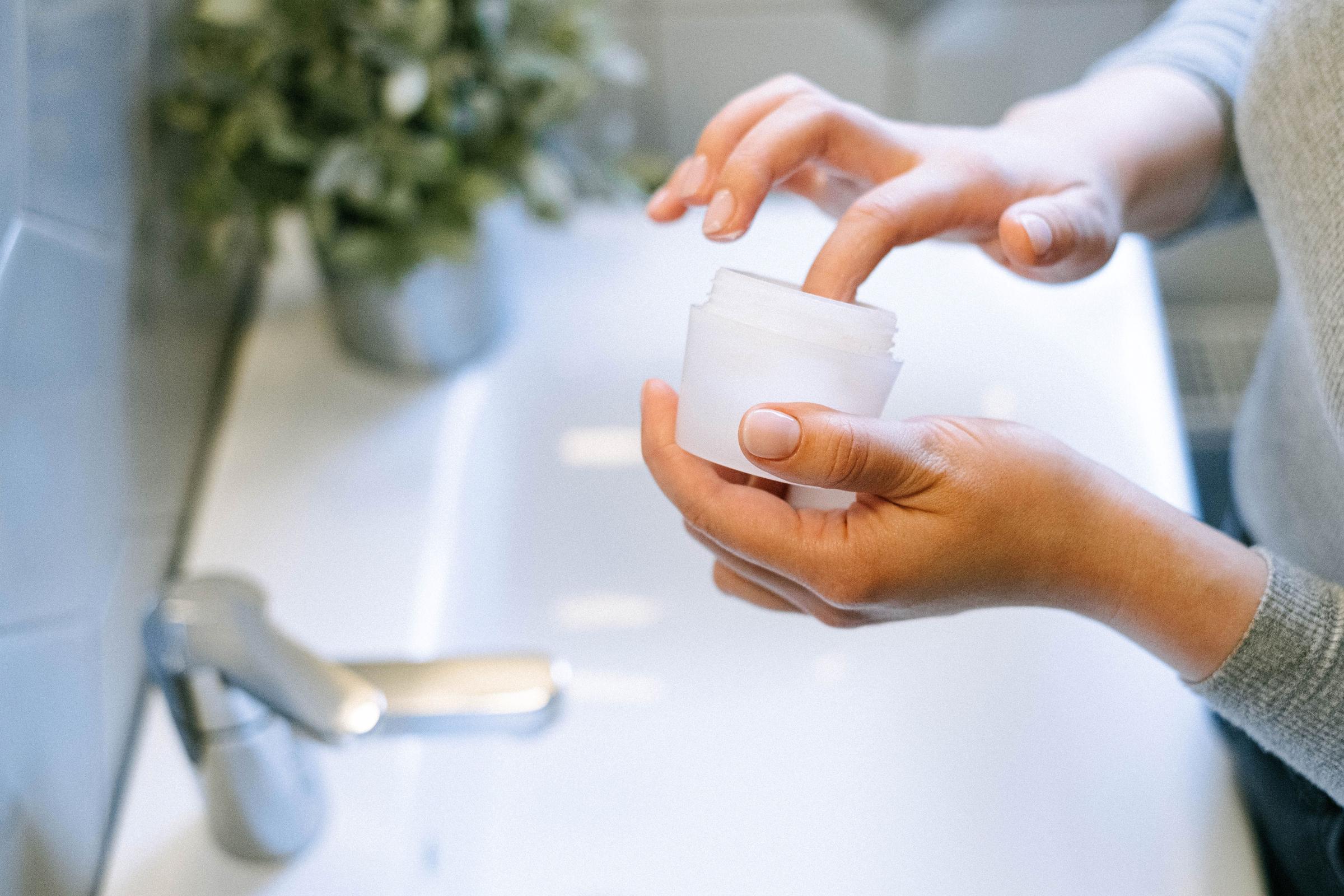 A person dipping their finger inside a skincare jar | Source: Pexels