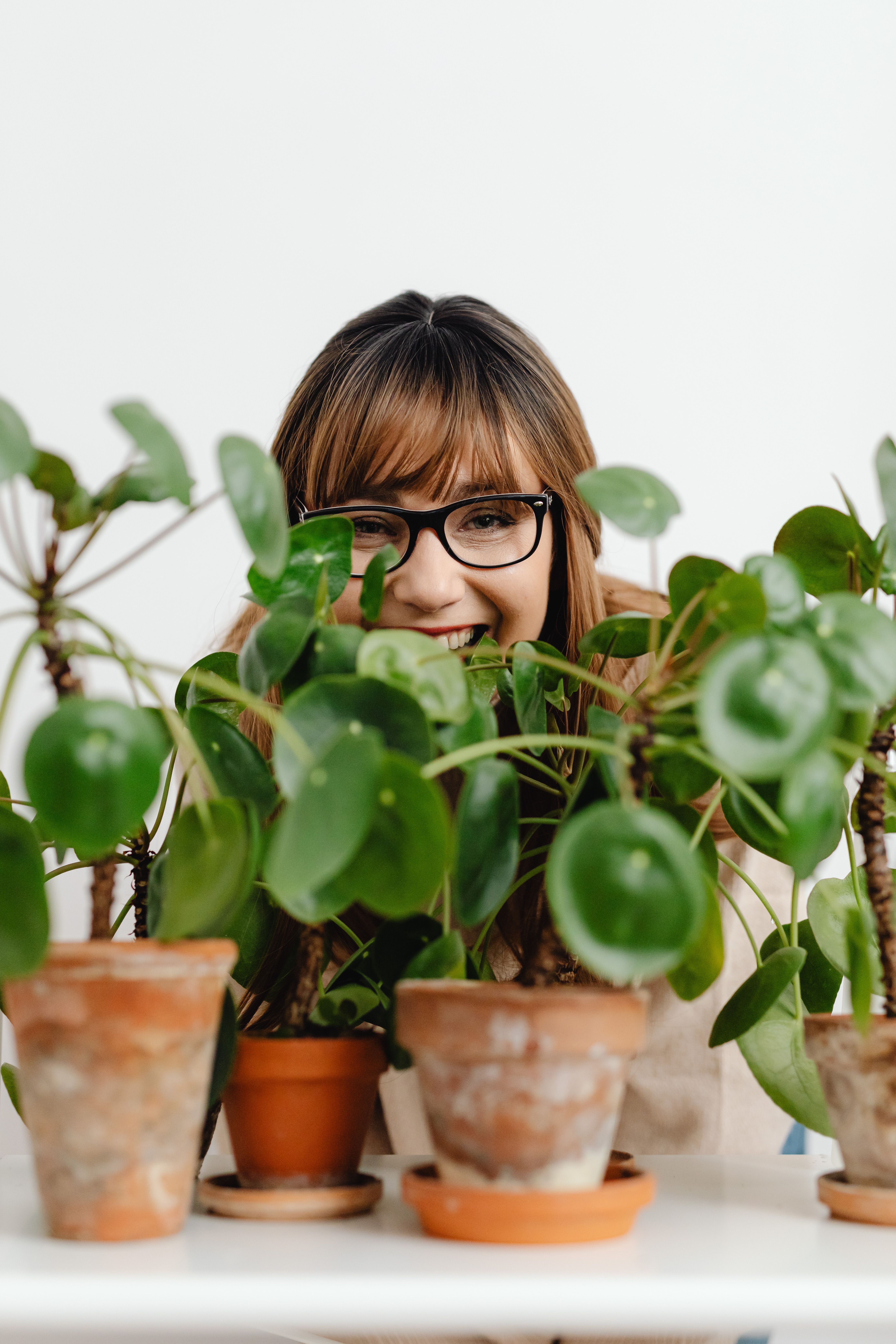 A woman smiling behind a row of indoor plants | Source: Pexels