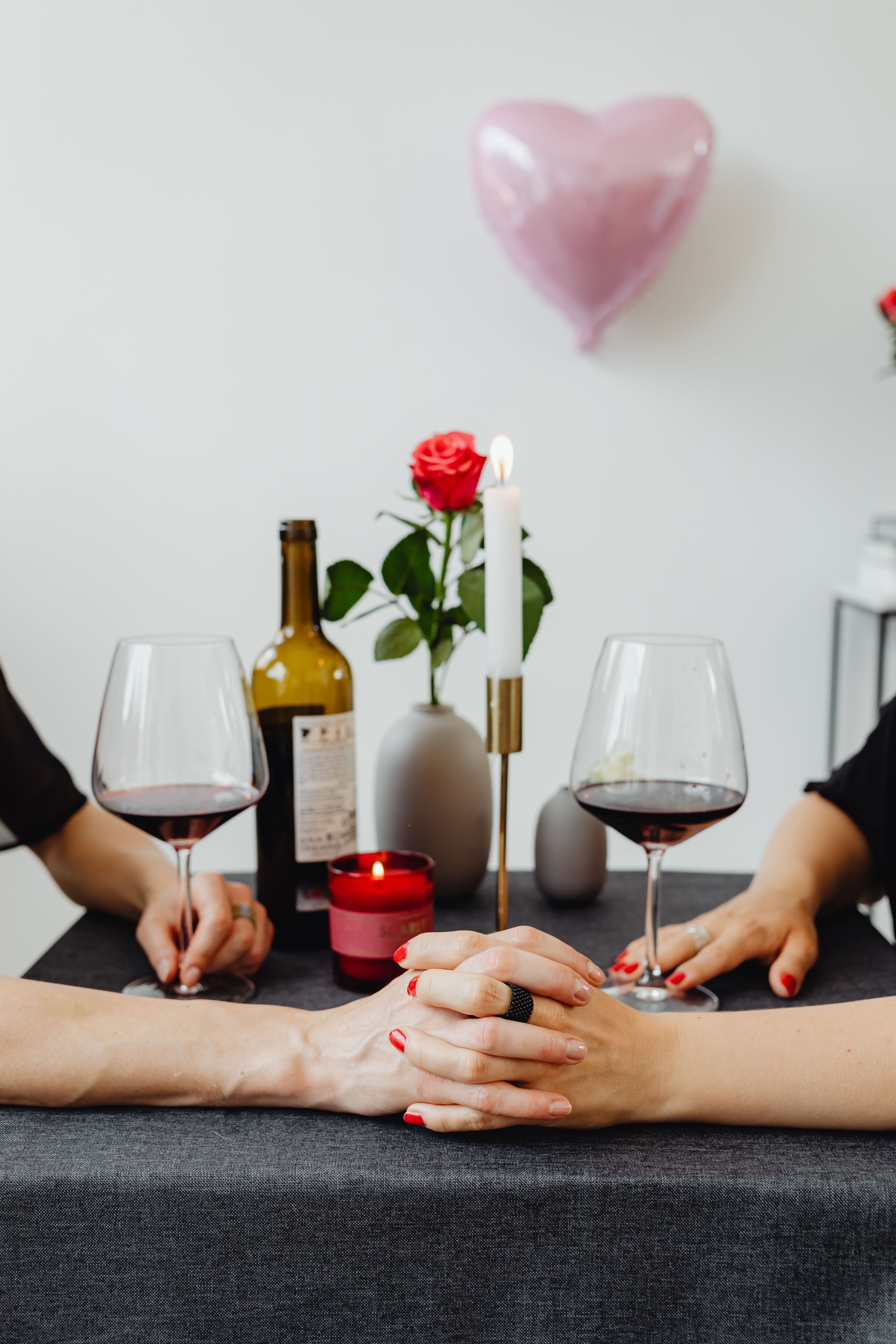 Woman with red nail polish holding hands with a man during a romantic dinner setting | Source: Pexles