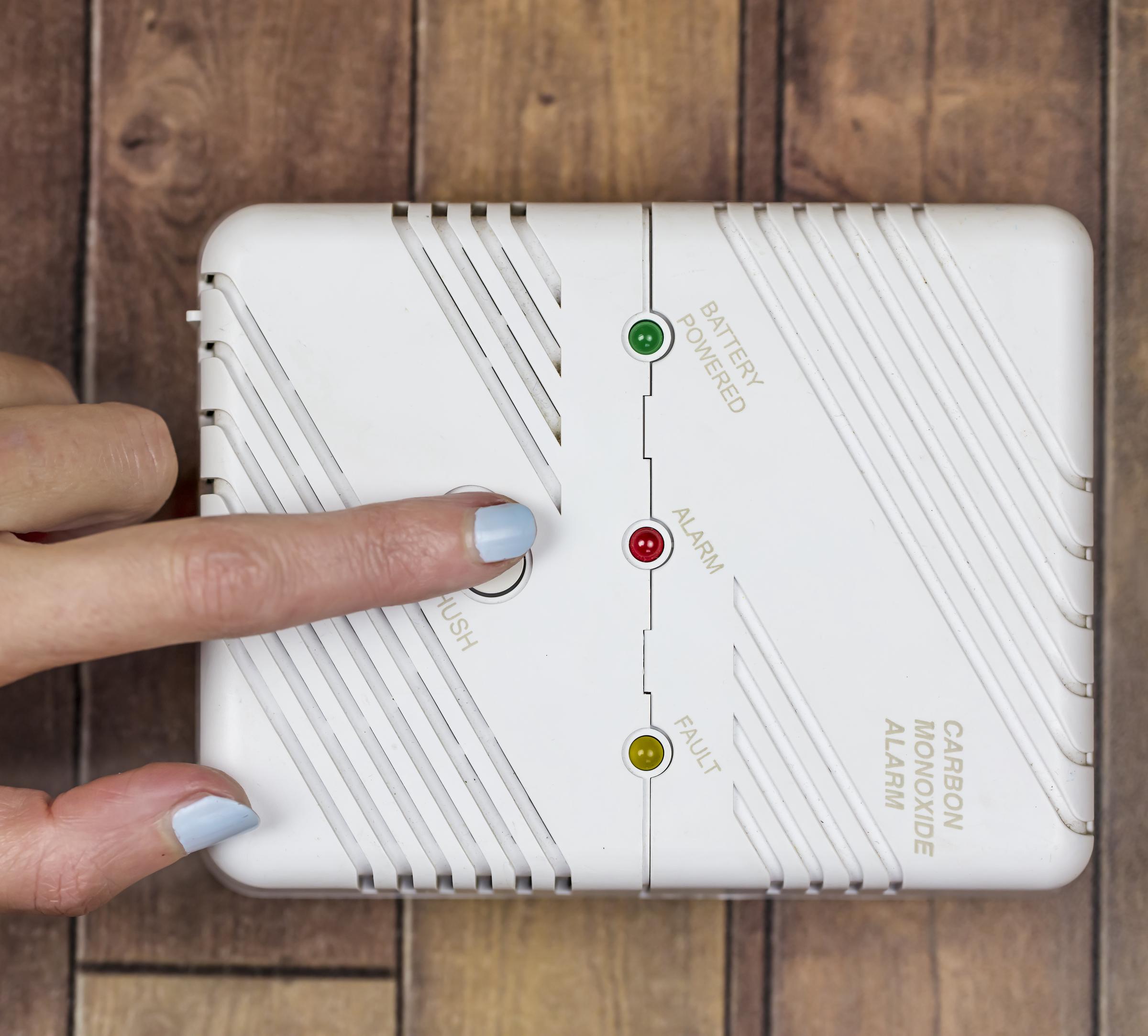 A hand punching the test button on an electrical carbon monoxide alarm | Source: Getty Images