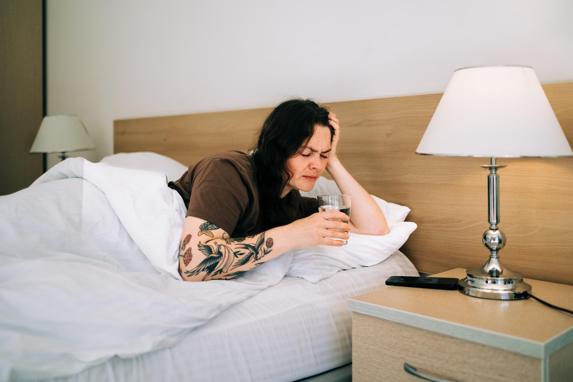 A sick woman drinking water from her bed | Source: Getty Images