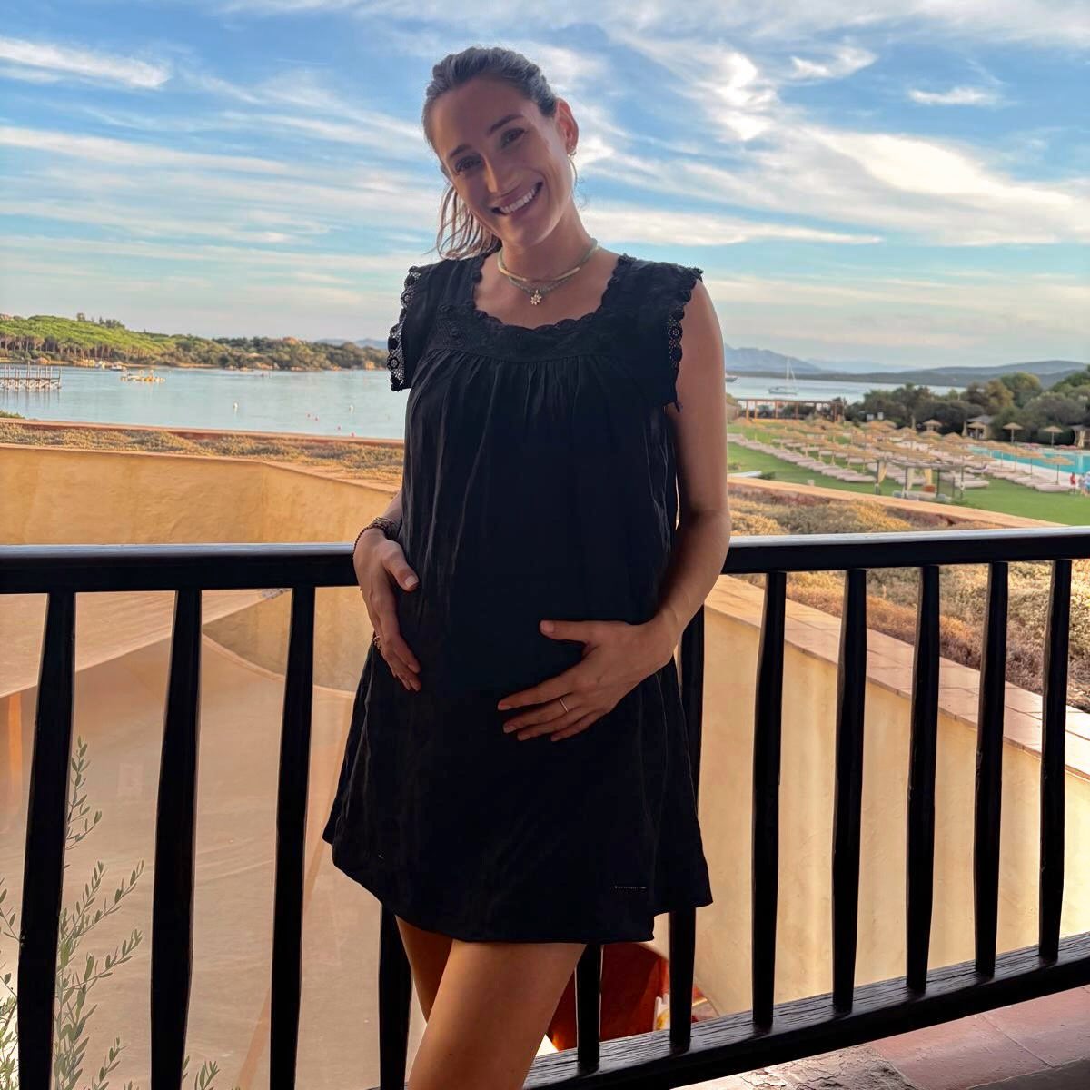 Jessica Springsteen cradles her growing baby bump while posing in a short black dress against a scenic waterfront backdrop. | Source: Instagram/jessicaspringsteen