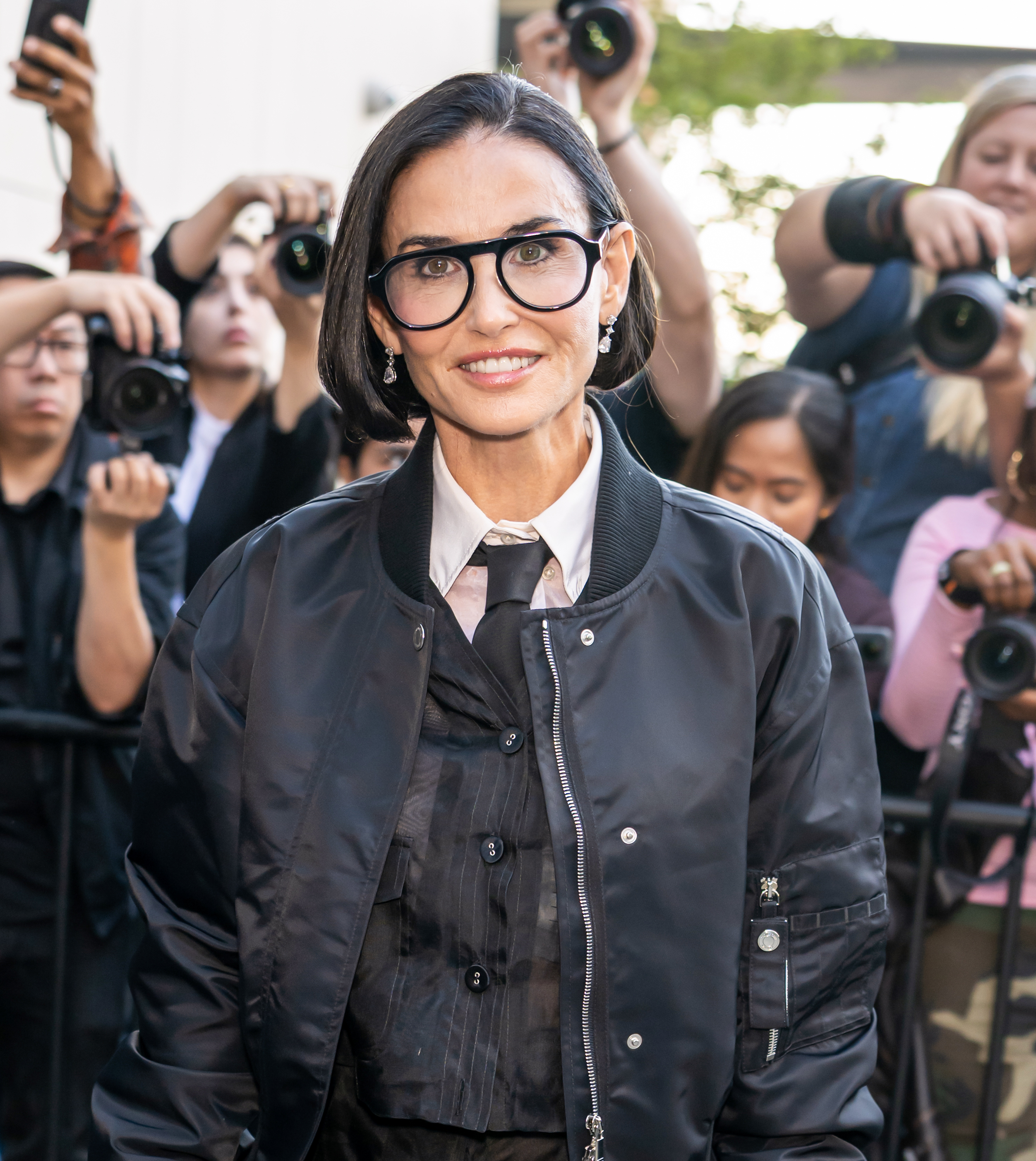 Demi Moore's sleek bob frames her face as she faces the cameras, with statement black glasses, sparkling drop earrings, and Thom Browne's layered tailoring completing her NYFW look. | Source: Getty Images