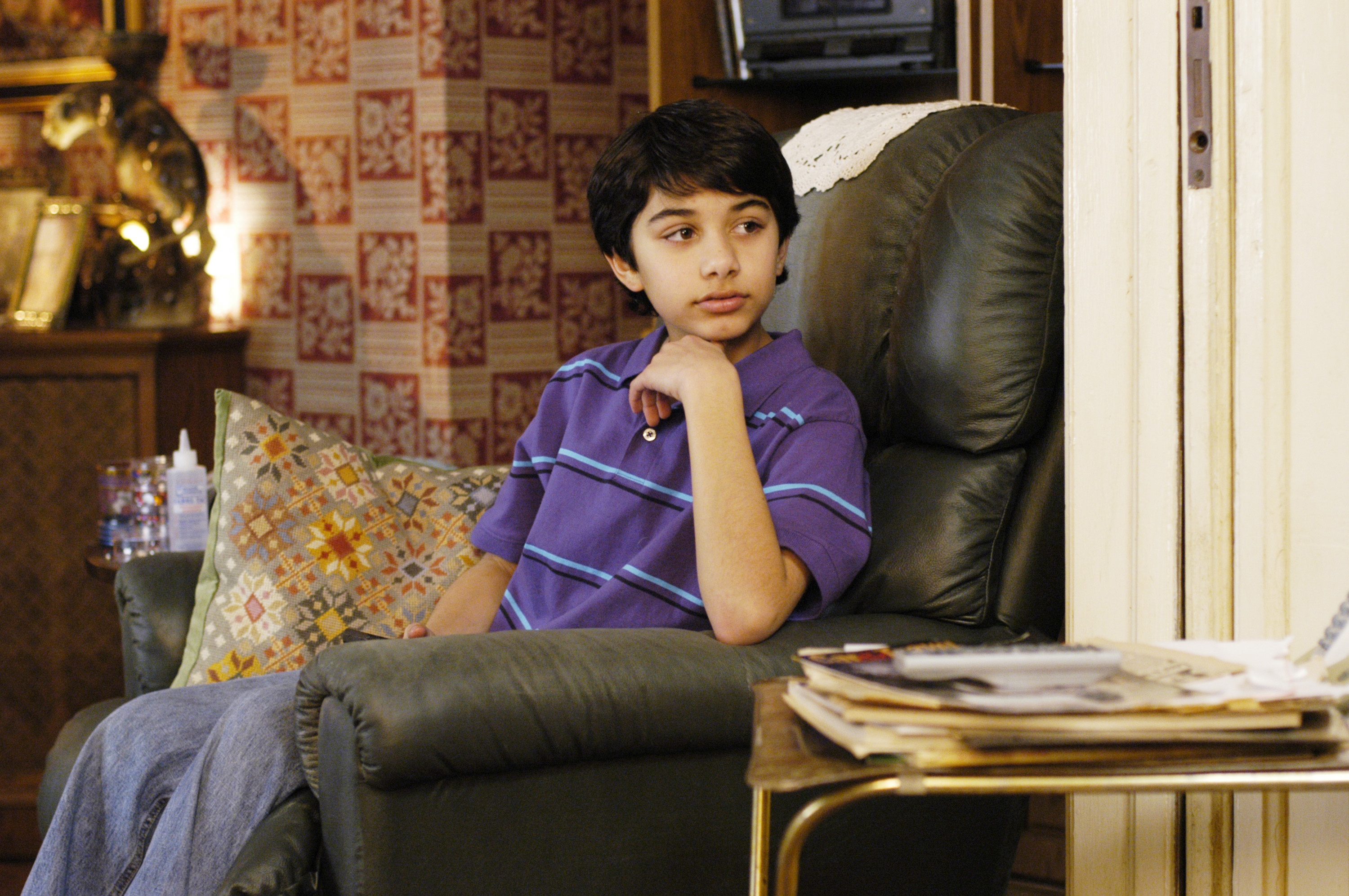 Mark Indelicato stars as Justin Suarez in the "Pilot" episode of the television series "Ugly Betty," photographed on April 26, 2005. Sitting thoughtfully in a green leather recliner with his hand propping up his chin, he looks off-camera wearing a bright purple striped polo shirt and blue jeans inside the warmly decorated Suarez family living room.