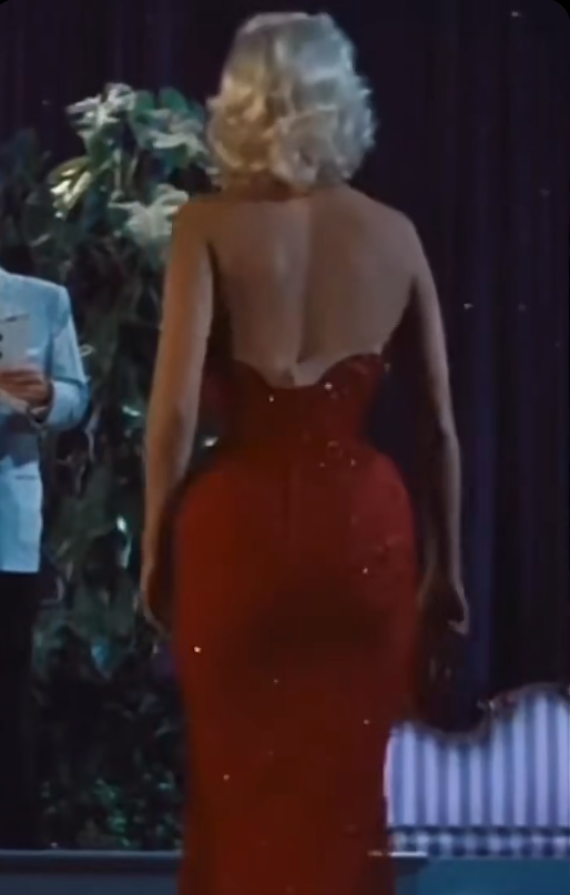Back Angle (The Girl Can’t Help It, 1956) A back-view frame highlighting the dramatic low-dipping V-back cut and hourglass waistline of Jayne Mansfield's iconic sparkling red dress. | Source: TikTok/@neciashairstyling