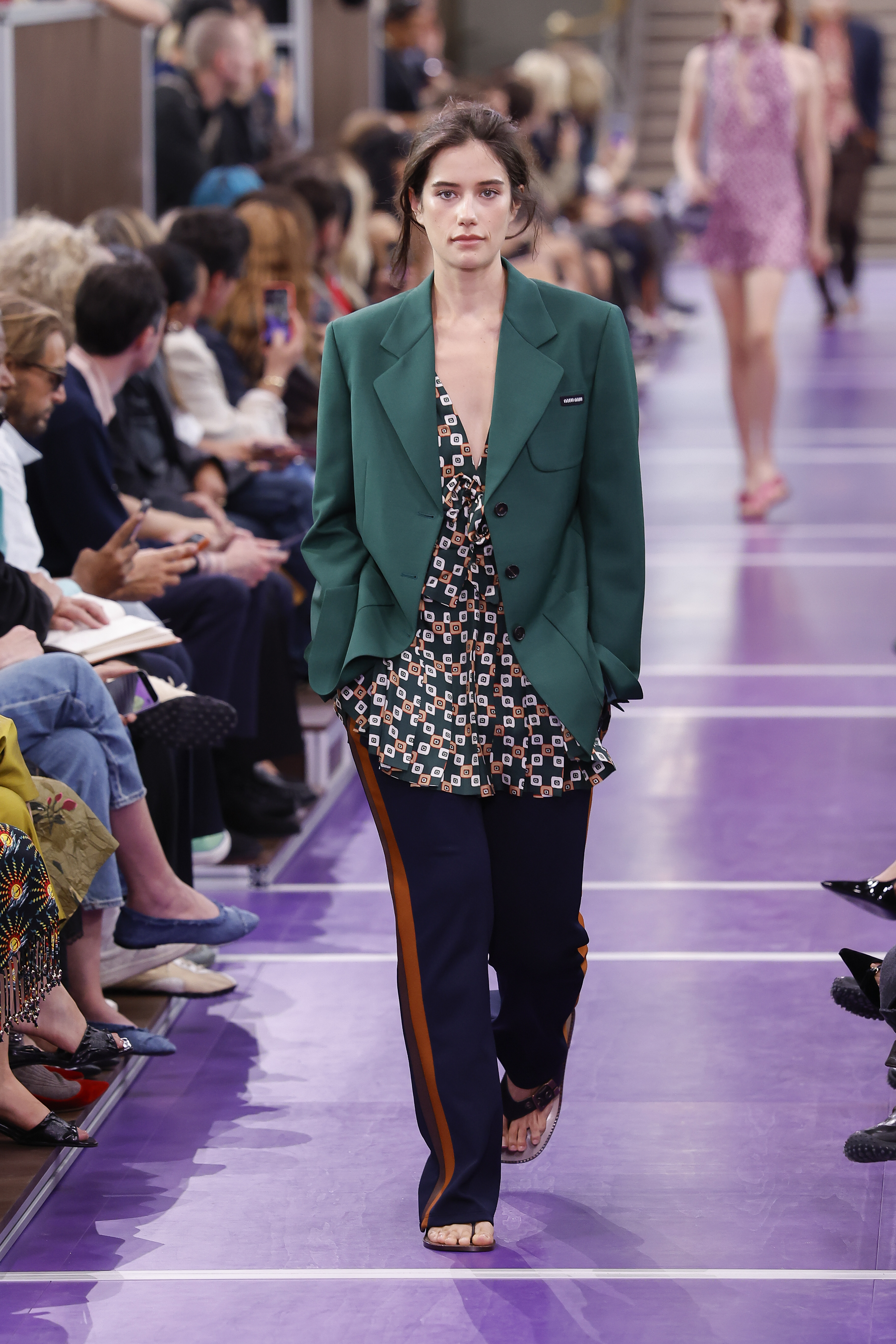 Ella Bleu Travolta takes another confident stride down the Miu Miu runway, with the packed audience lining the purple catwalk as she showcases the statement look from a different angle. | Source: Getty Images