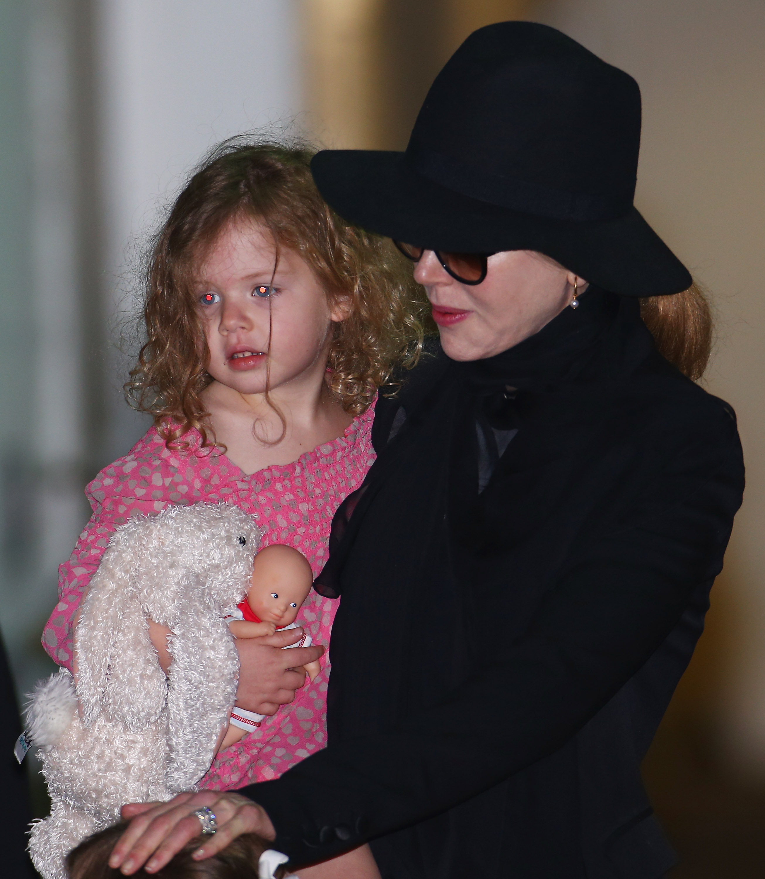 Nicole Kidman carries her three-year-old daughter Faith Margaret during a family trip in January 2014. Faith clutches a stuffed bunny and a baby doll while her mother keeps her close. | Source: Getty Images