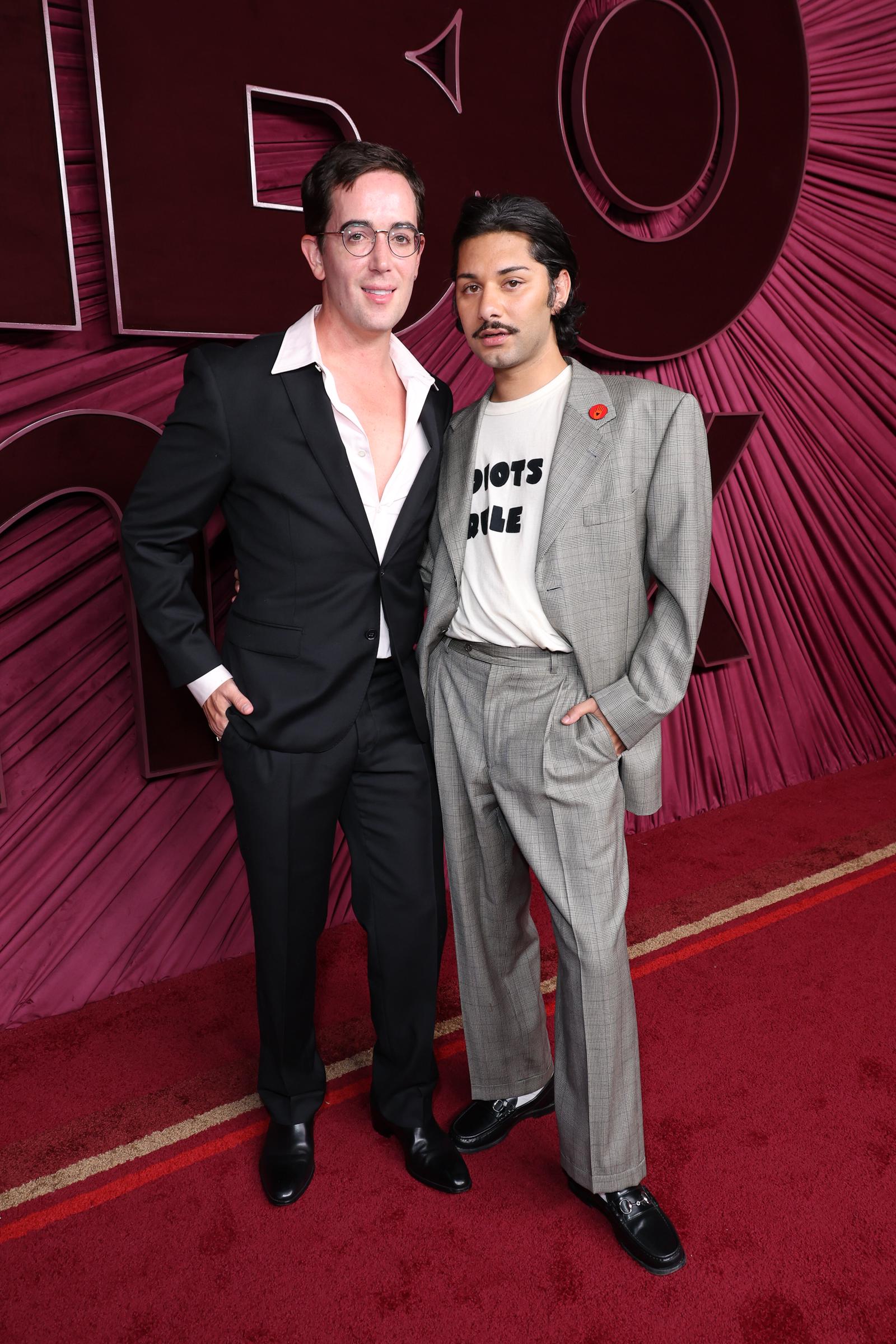 Mark Indelicato and partner David Watson share a close moment in the arrivals area of the HBO Max Primetime Emmy Awards afterparty at San Vicente Bungalows on September 14, 2025, in Los Angeles, California. Framing both from the waist up, Watson flashes a gentle smile with his collar wide open, while Indelicato fixes a direct gaze on the photographer, highlighting his styled dark hair, thin mustache, and the Artists4Ceasefire pin pinned neatly to his lapel.