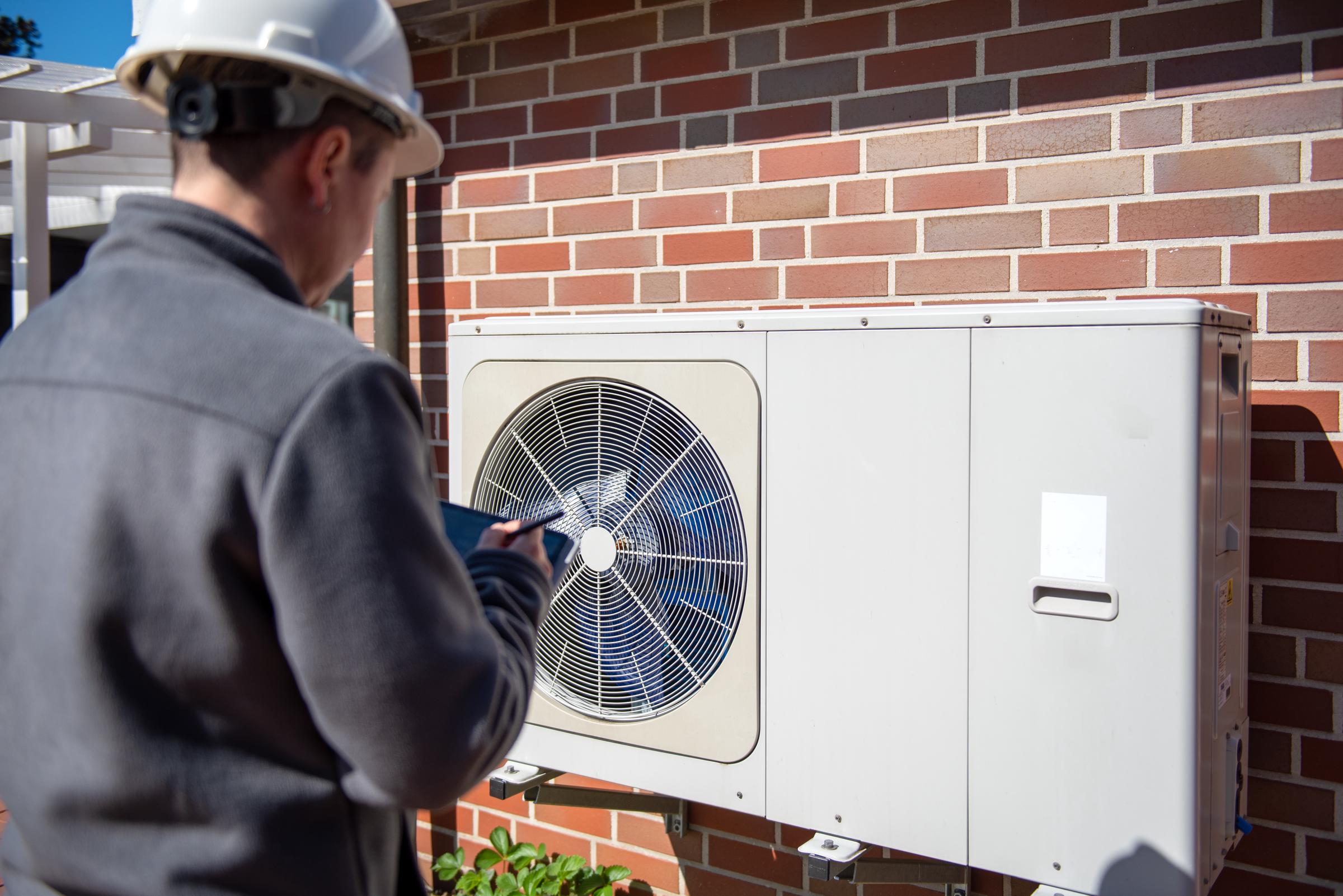 A technician inspecting an HVAC unit mounted on a brick wall | Source: Getty Images