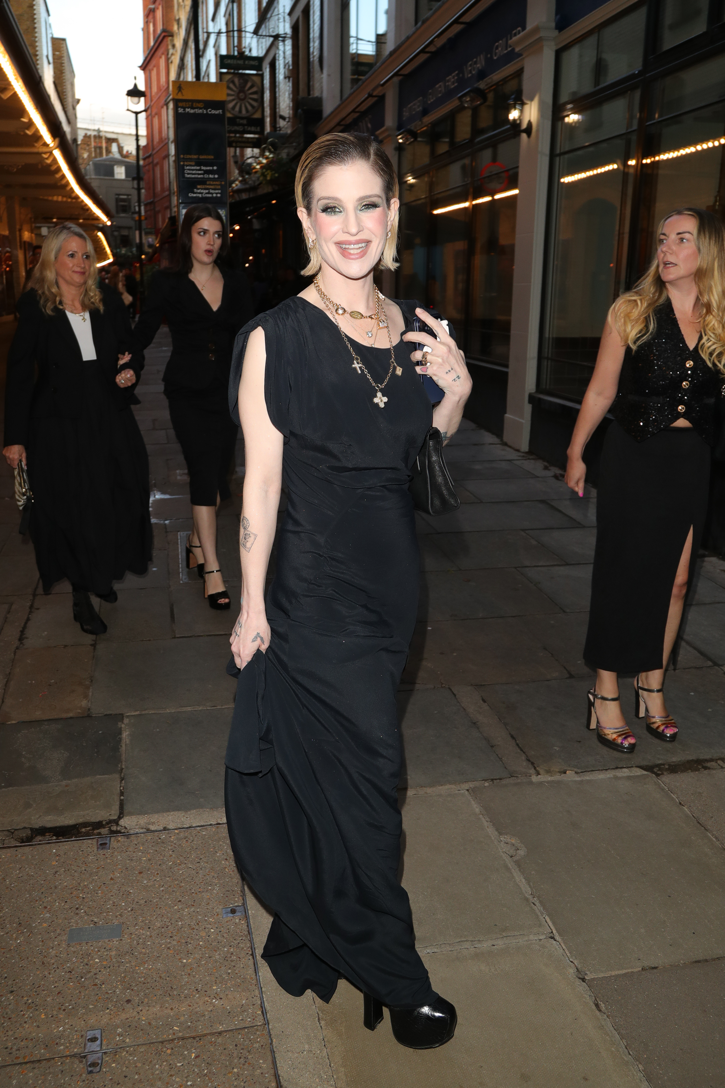 Kelly Osbourne smiled for photographers during an outing in London, wearing a long black gown, layered cross necklaces, and a sleek, swept-back hairstyle. | Source: Getty Images.