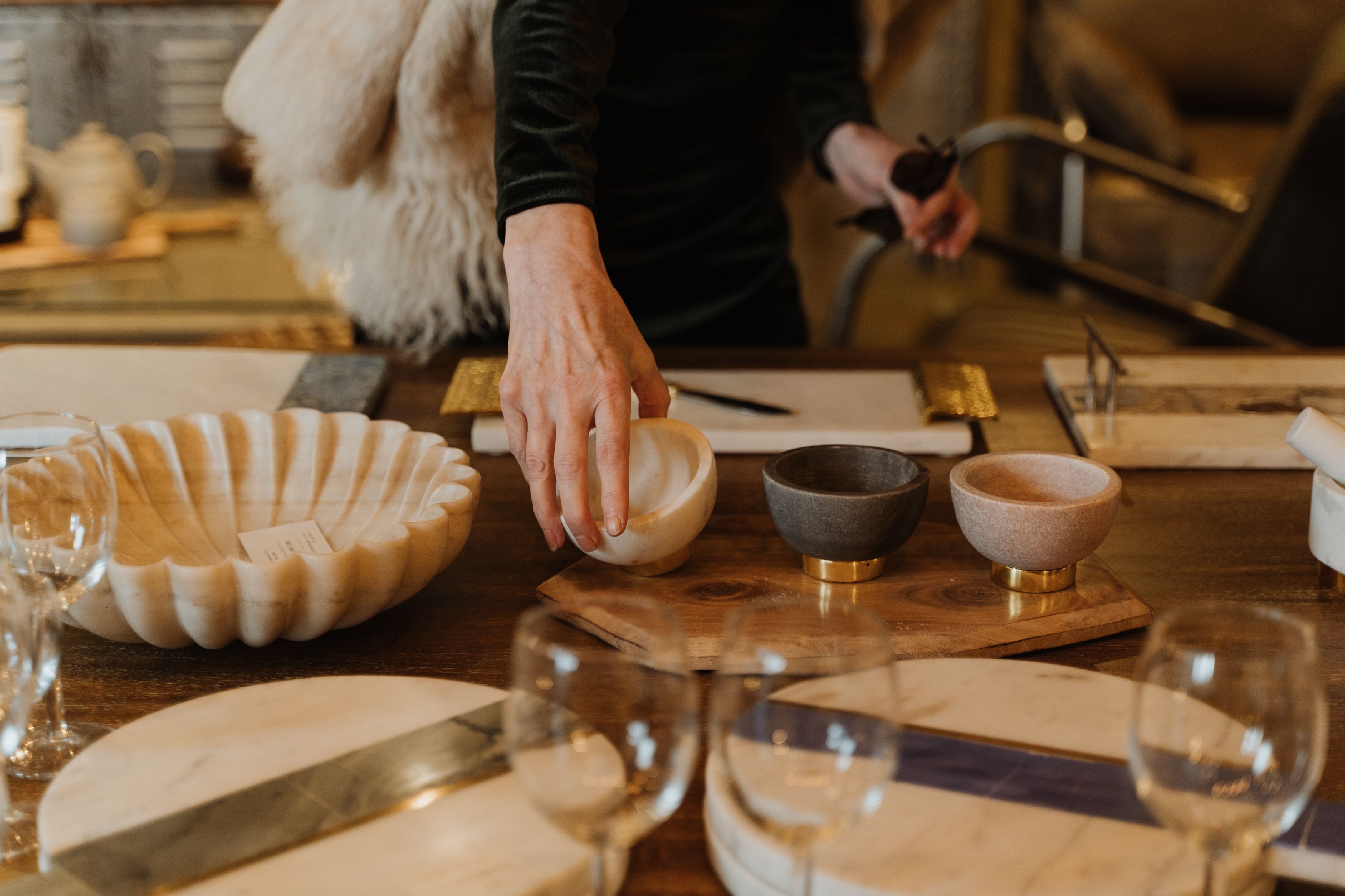 A person arranges decorative bowls on a wooden dining table. | Source: Pexels