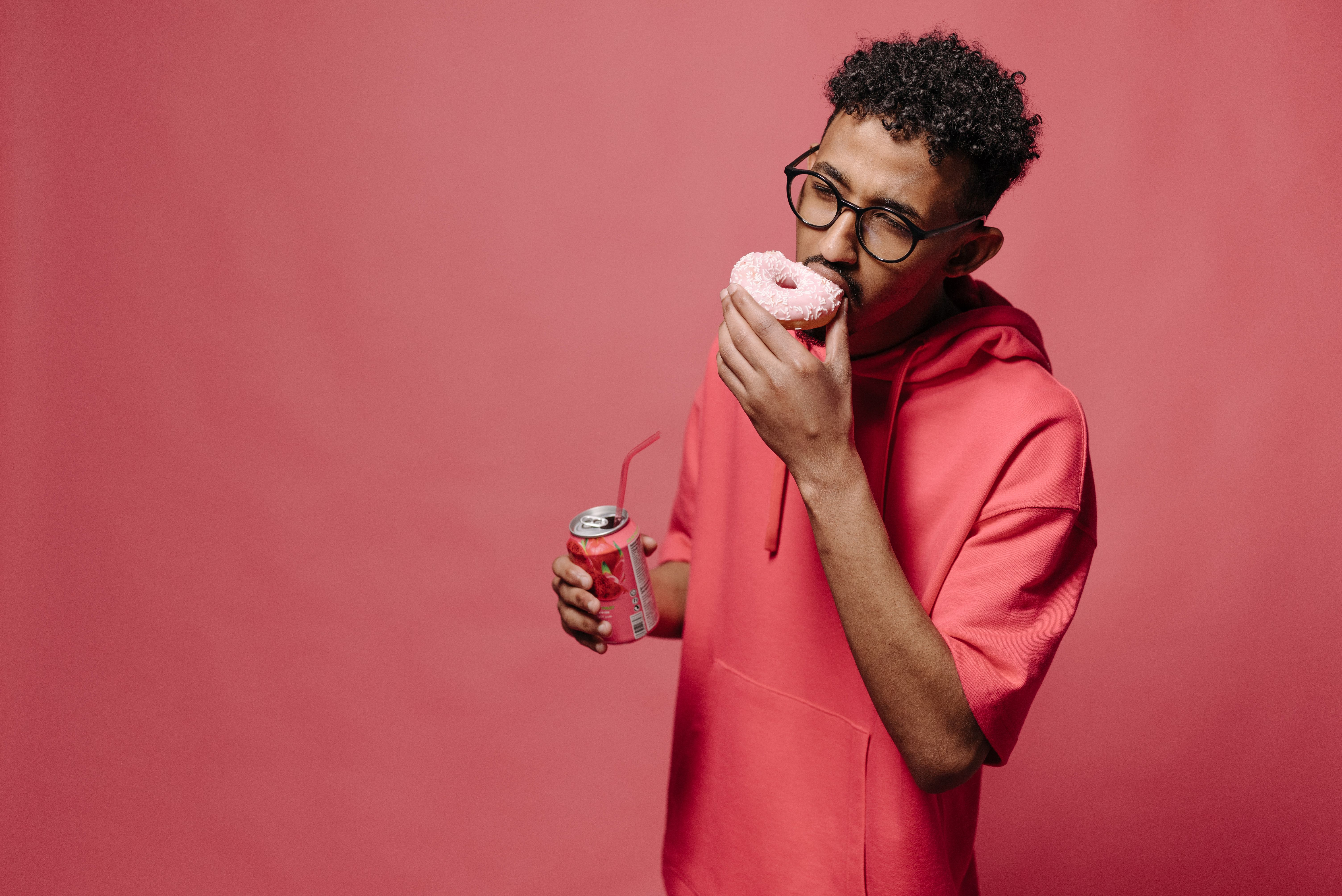 A man eating a donut and holding a can of juice | Source: Pexels