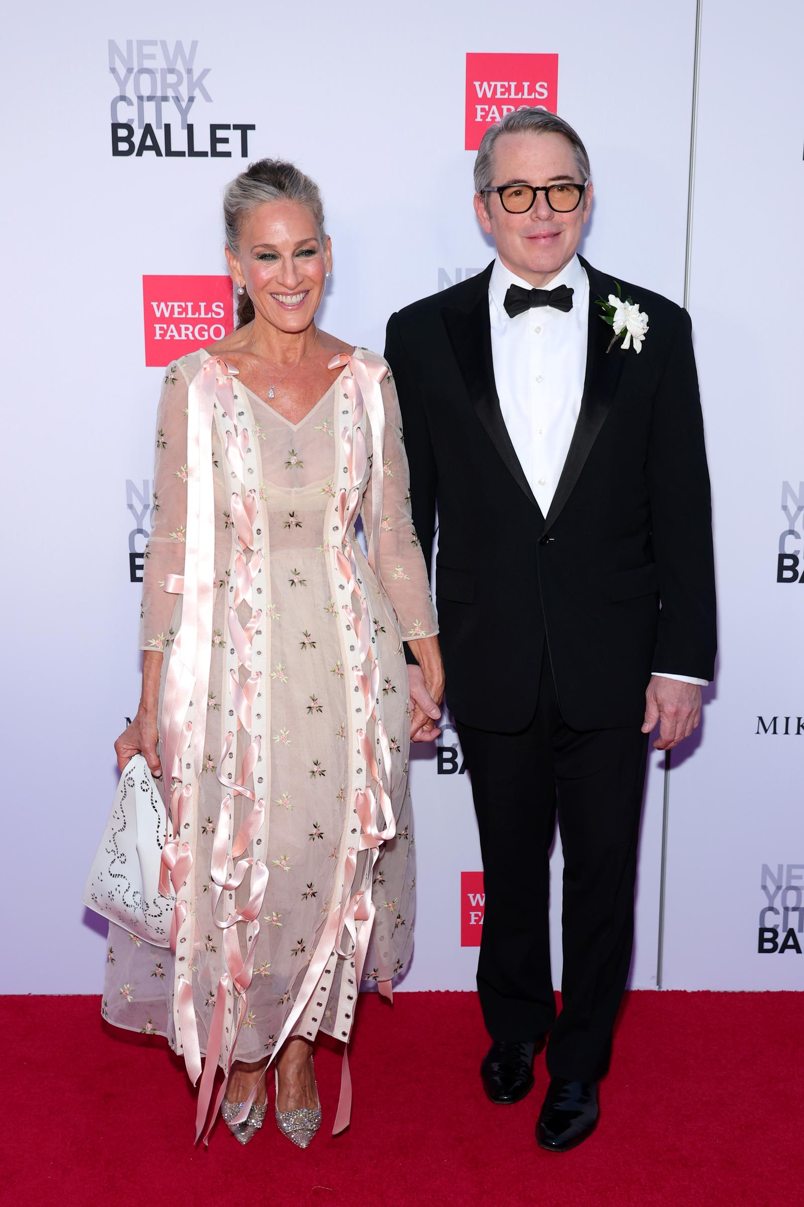 Sarah Jessica Parker holds hands with Matthew Broderick as her semi-sheer floral gown, trailing pink ribbons, sparkling heels, and white handbag come fully into view. | Source: Getty Images