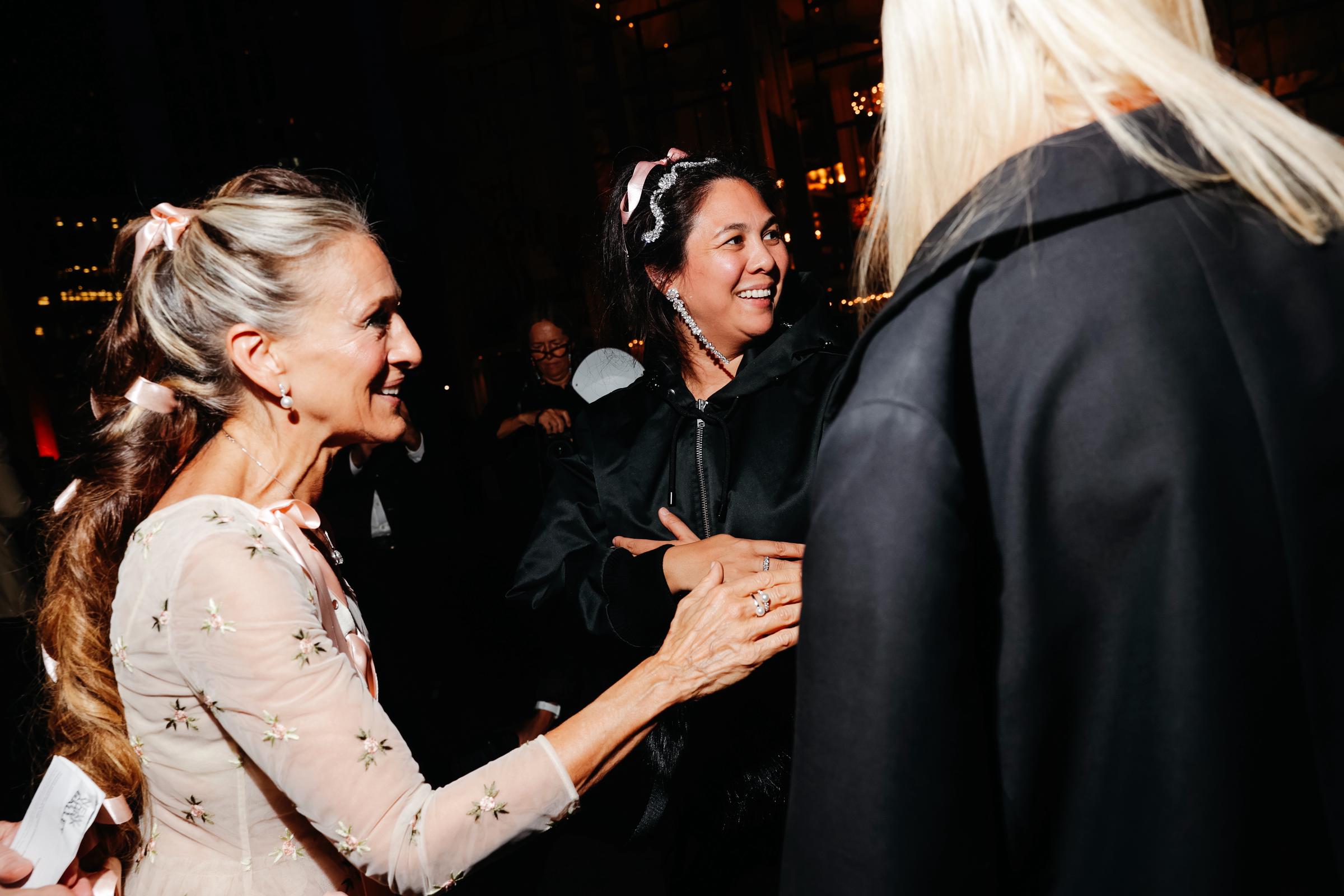 Sarah Jessica Parker mingles with designer Simone Rocha, in New York City, with pink ribbons offering a subtle preview of Parker's elaborate look. | Source: Getty Images
