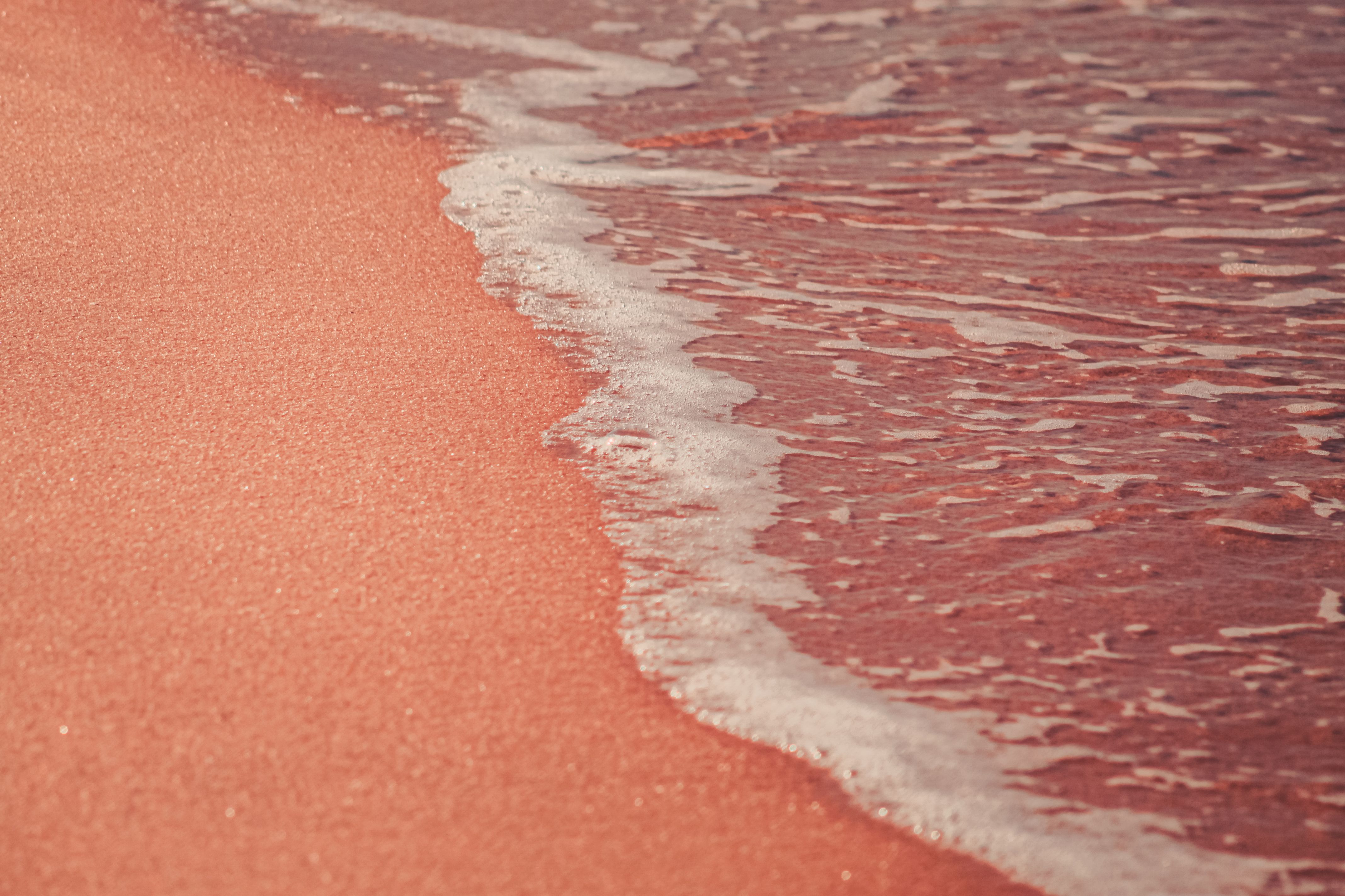 A close-up of a wave washing onto pink sand. | Source: Pexels