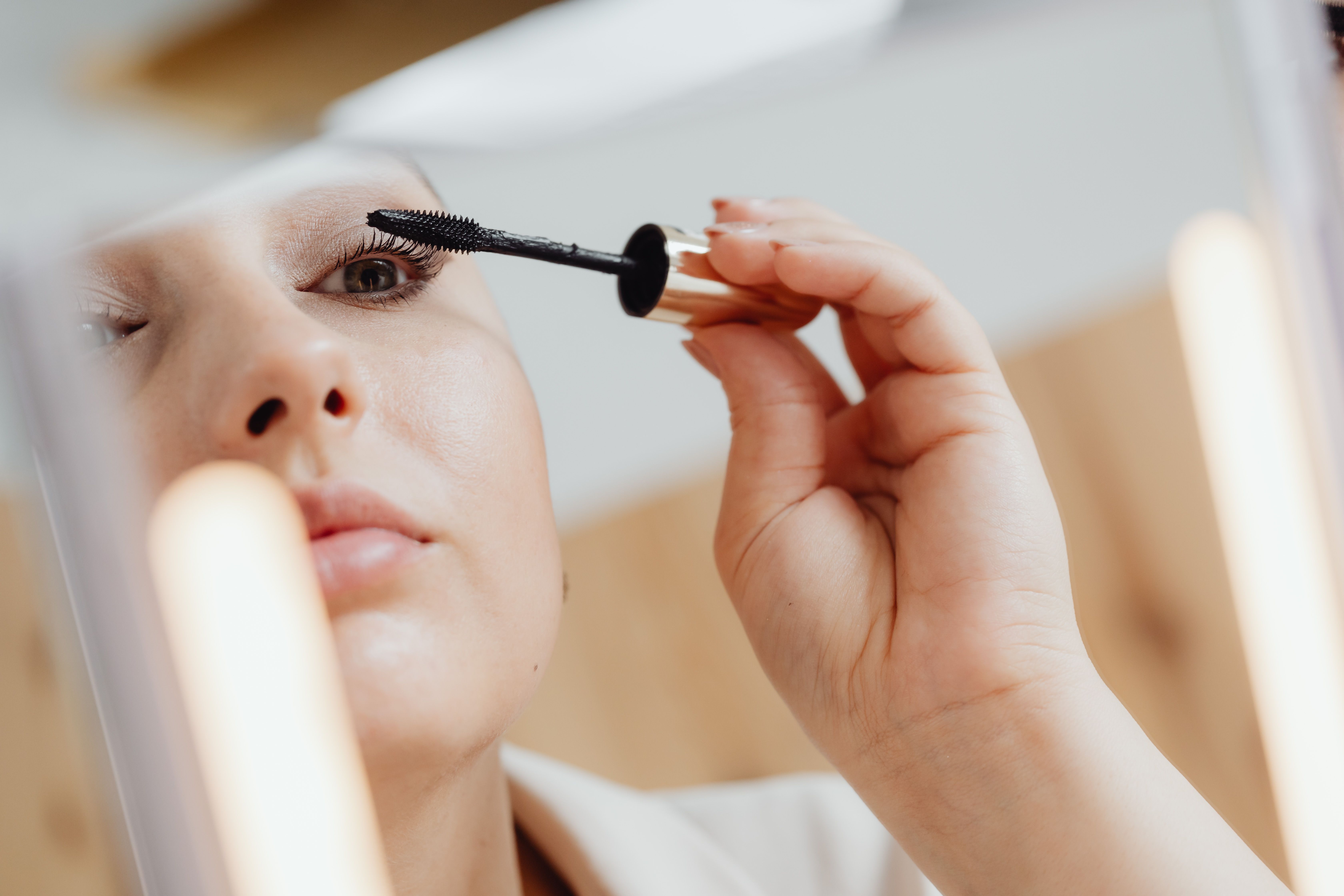 A woman's reflection on a mirror as she applies mascara on her lashes | Source: Pexels