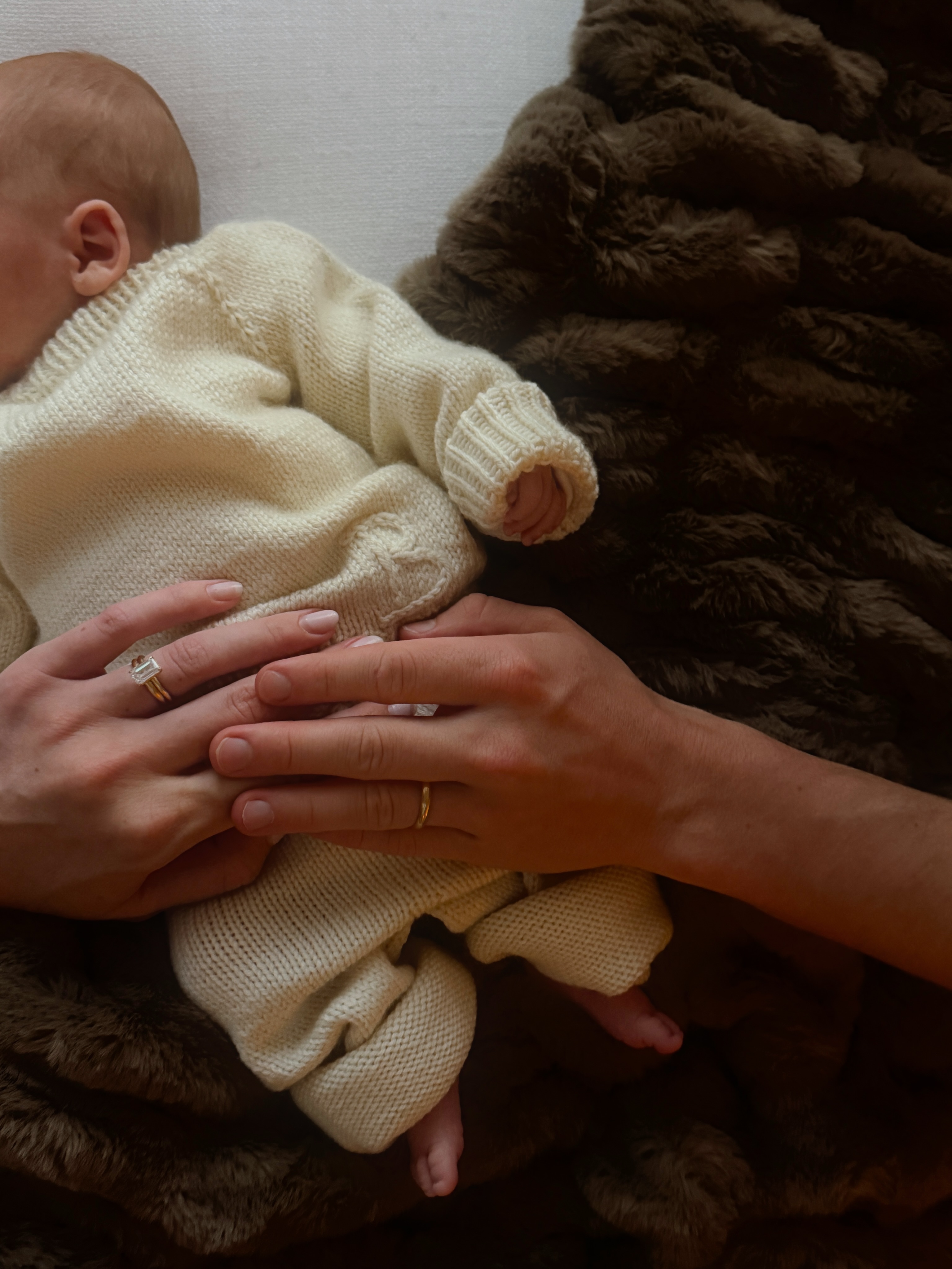 Baby Bond Leo Bure rests in a cream knit outfit as his parents place their hands around him, their wedding rings visible in the close-up family photo. | Source: Instagram/elliottpbure
