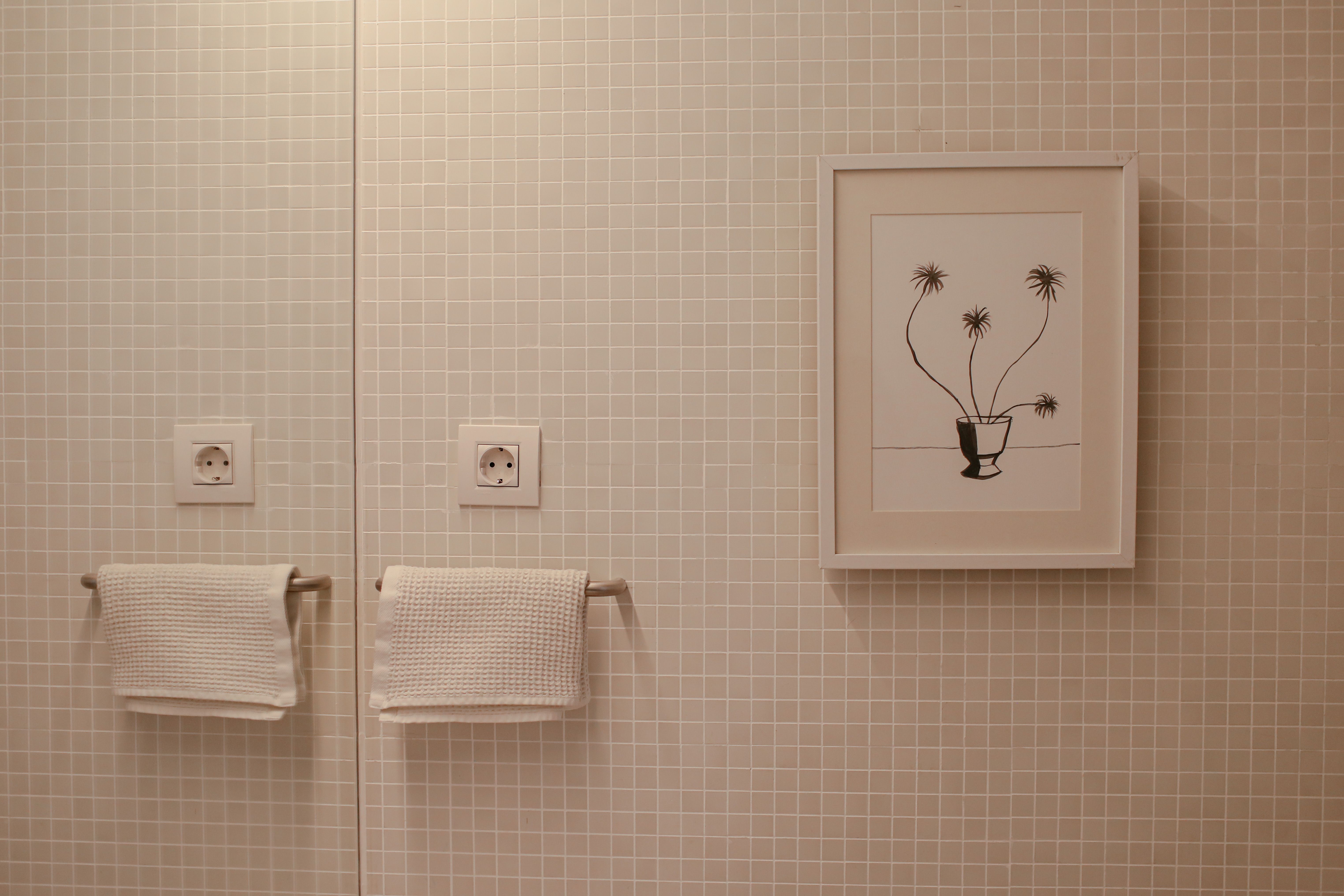 A tiled bathroom wall decorated with framed artwork and white towels. | Source: Pexels
