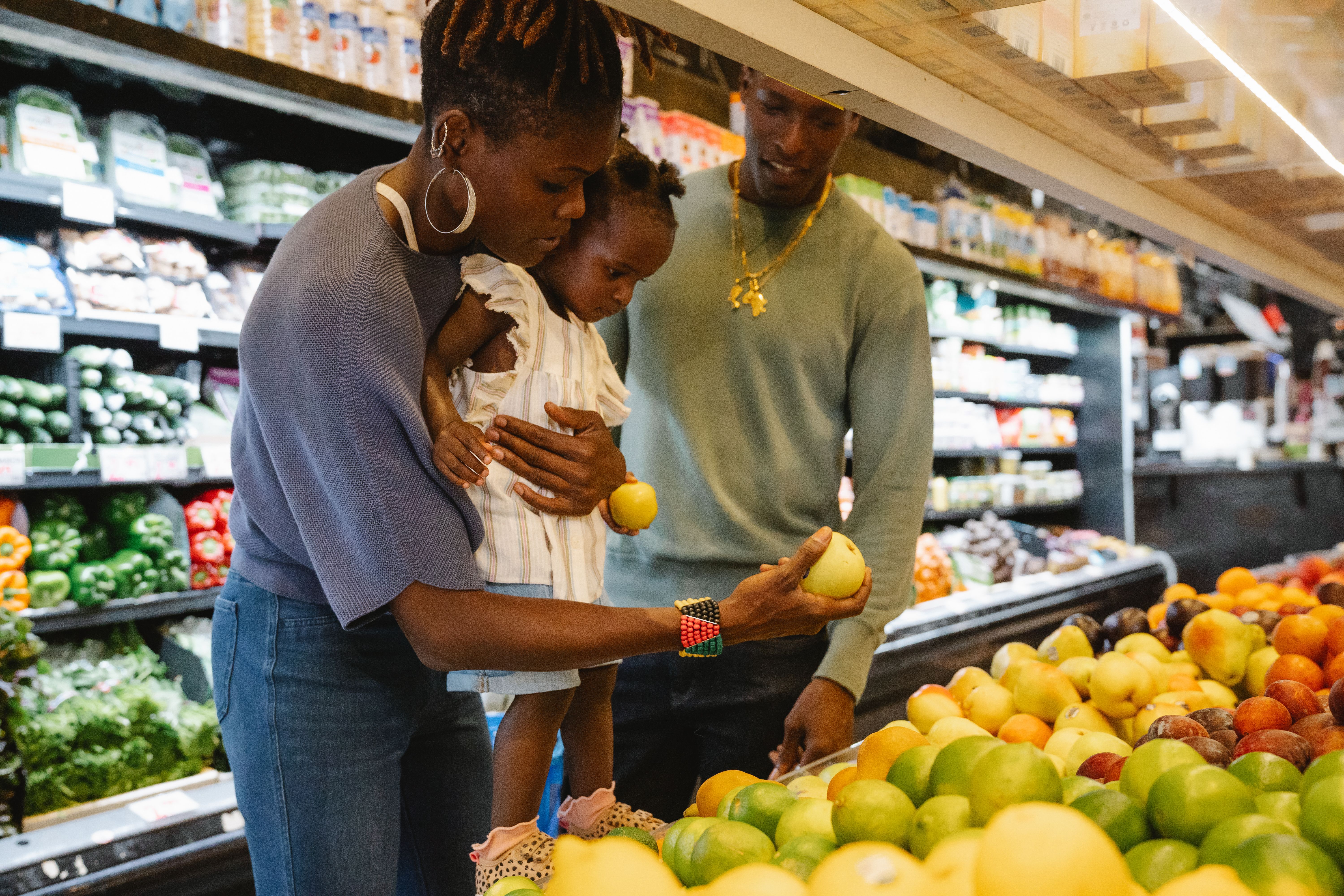 A couple showing their toddler some fruits at the grocery store | Source: Pexels