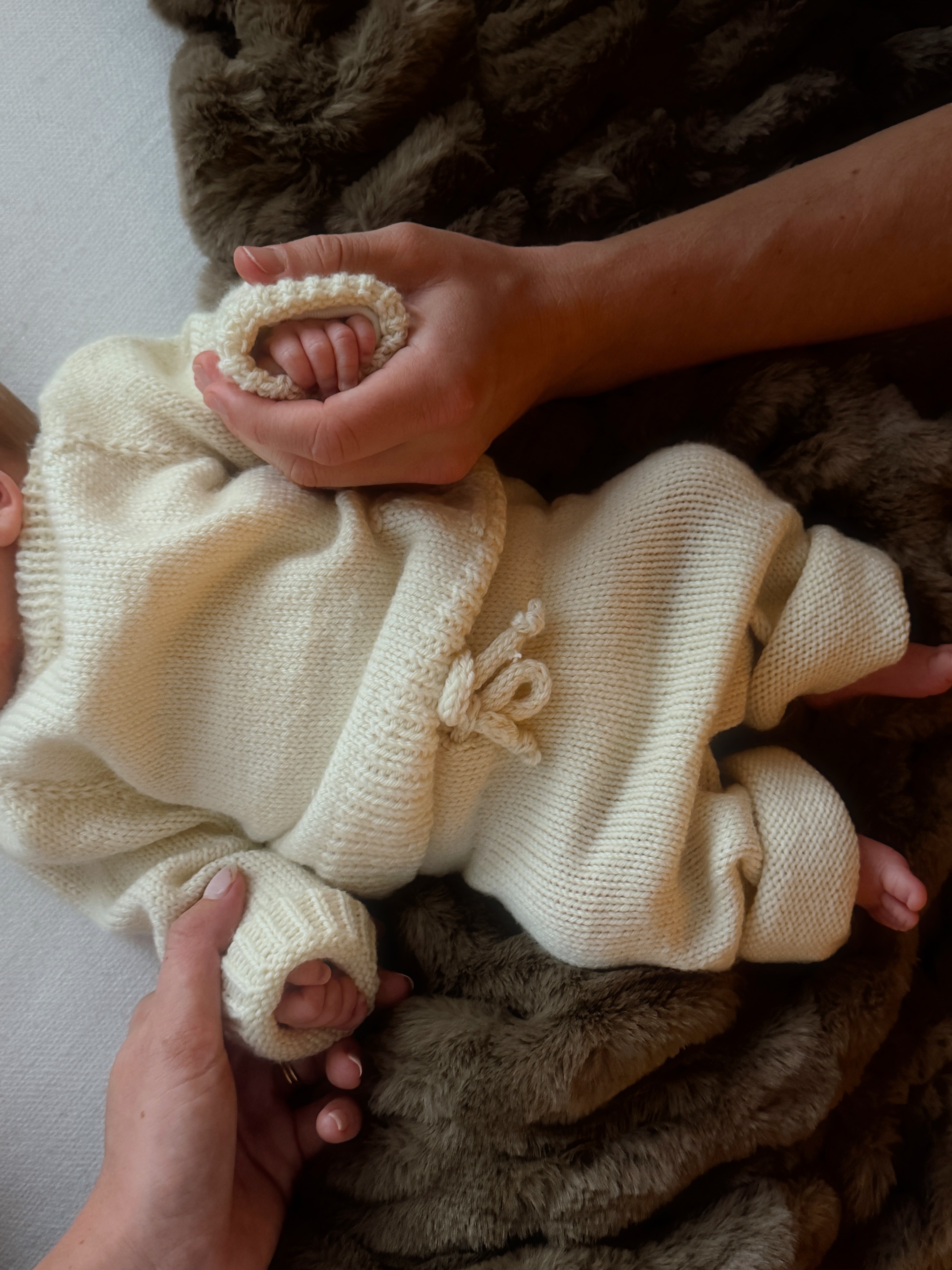 Bond's tiny hands peek from the sleeves of his cream knit outfit while his parents cradle them in their palms at home. | Source: Instagram/elliottpbure