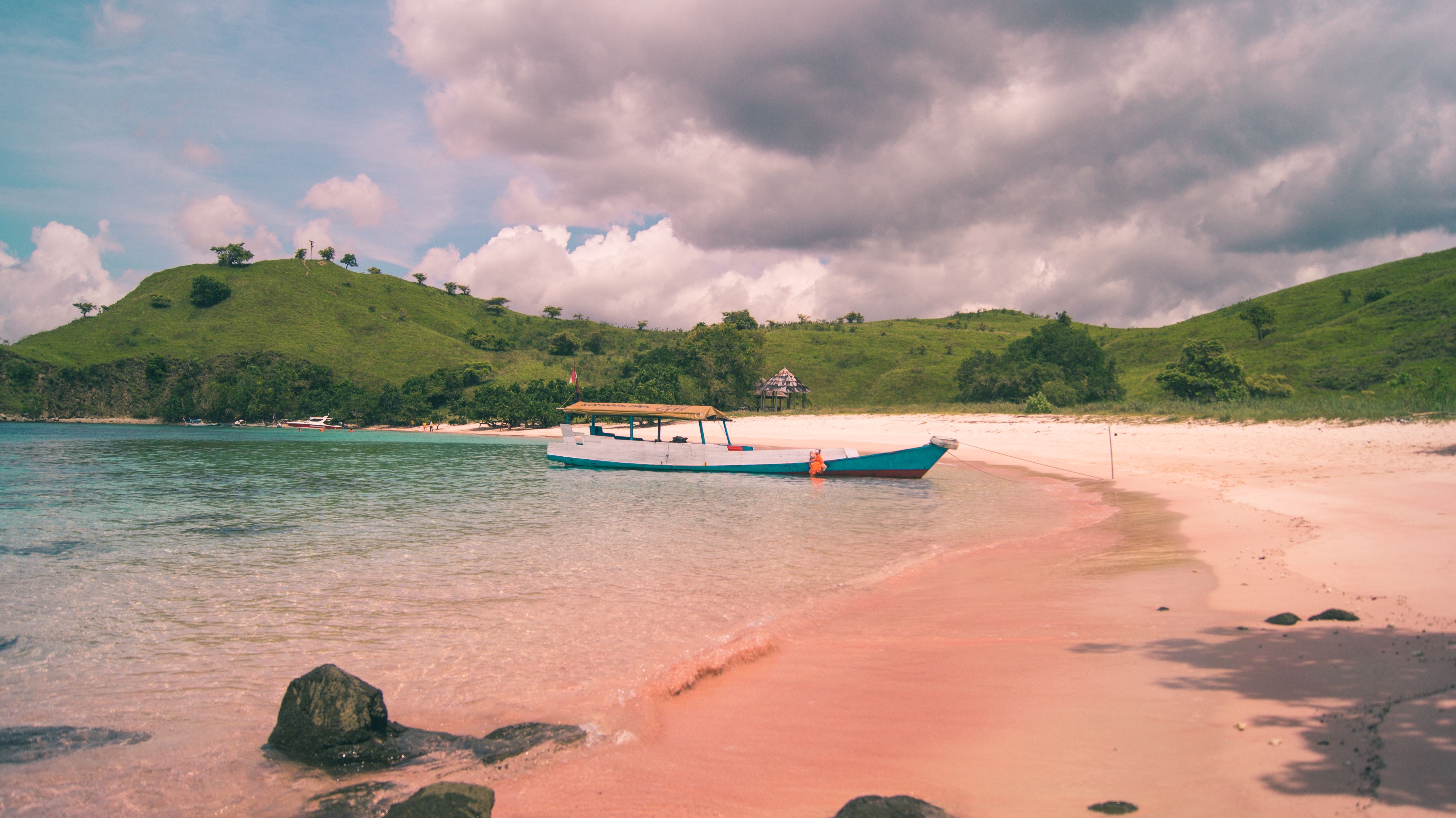 A boat sits in shallow water beside a pink sand beach, with green hills behind it. | Source: Pexels