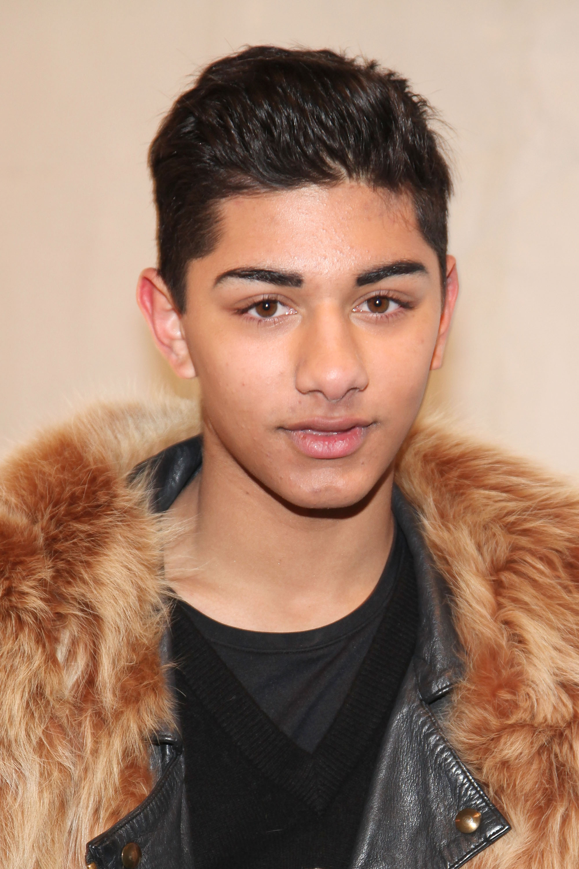Mark Indelicato poses backstage at the Duckie Brown Fall 2011 fashion show during Mercedes-Benz Fashion Week at The Studio at Lincoln Center on February 10, 2011, in New York City. Looking directly into the camera with styled dark hair, he layers an oversized brown fur stole over a black leather biker jacket and a black V-neck top.