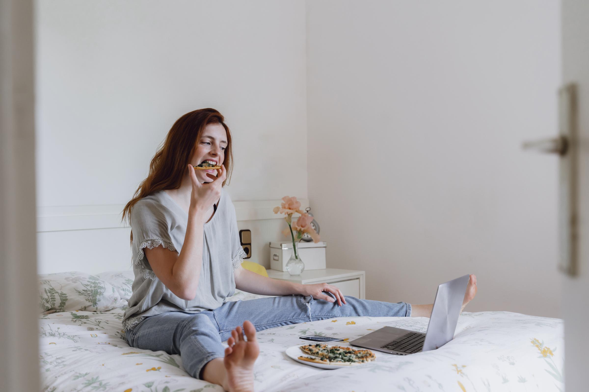 A woman eating pizza on her bed while watching a movie on her laptop | Source: Getty Images