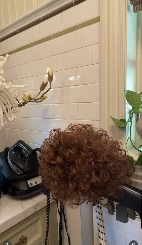 Another of McCarthy’s wigs is shown drying beside the sink, revealing its full, tightly curled style. | Source: Instagram/melissamccarthy