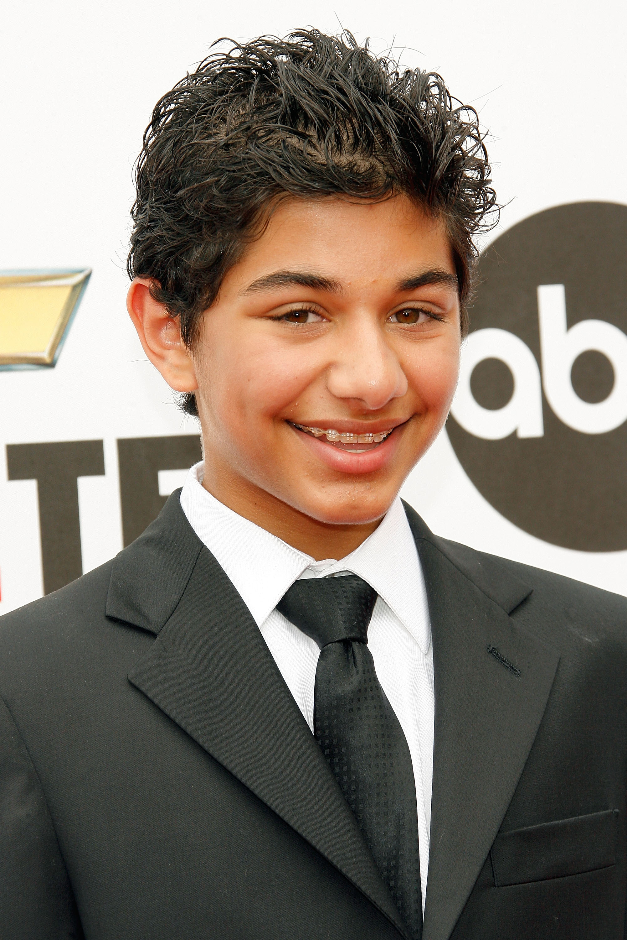 Mark Indelicato smiles in a close-up portrait arriving at the 2007 NCLR ALMA Awards held at the Pasadena Civic Auditorium on June 1, 2007, in Pasadena, California. Styled with curly, gelled dark hair and displaying his braces, he looks sharp in a tailored black suit jacket paired with a crisp white dress shirt and a textured black tie against an ABC and sponsor step-and-repeat backdrop.