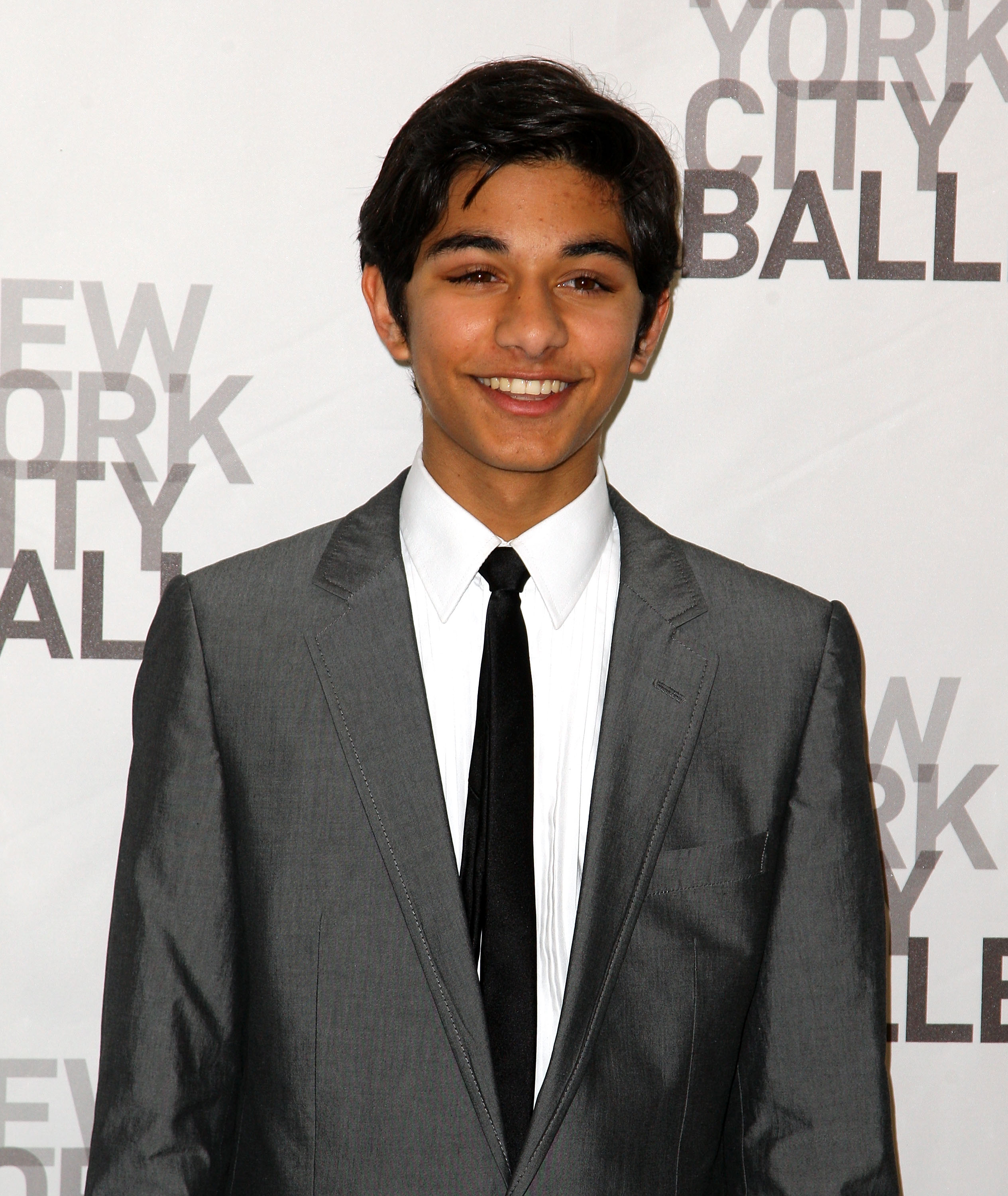 Mark Indelicato smiles in a tailored suit at the opening night celebration of the New York City Ballet at David H. Koch Theater, Lincoln Center, on November 25, 2008, in New York City. He wears a sharp grey two-button suit jacket paired with a crisp white dress shirt and a slim black necktie, posing against the event's step-and-repeat backdrop.
